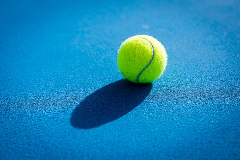 Tennis ball bouncing against vibrant blue background creating dynamic shadows in motion sequence.
