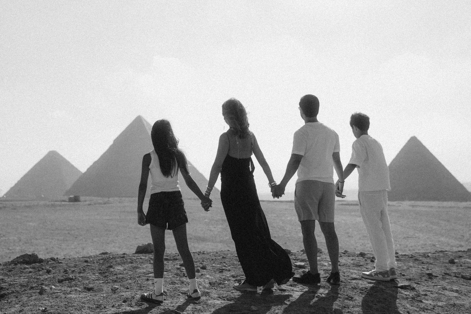 Silhouetted group of travelers sits together overlooking the ancient pyramids of Giza in the misty distance.