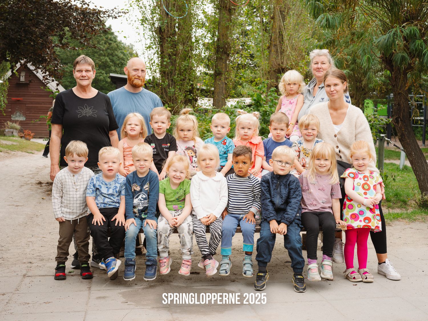 Group of children sitting on wooden logs in a sunny outdoor forest setting for a spring photo shoot.