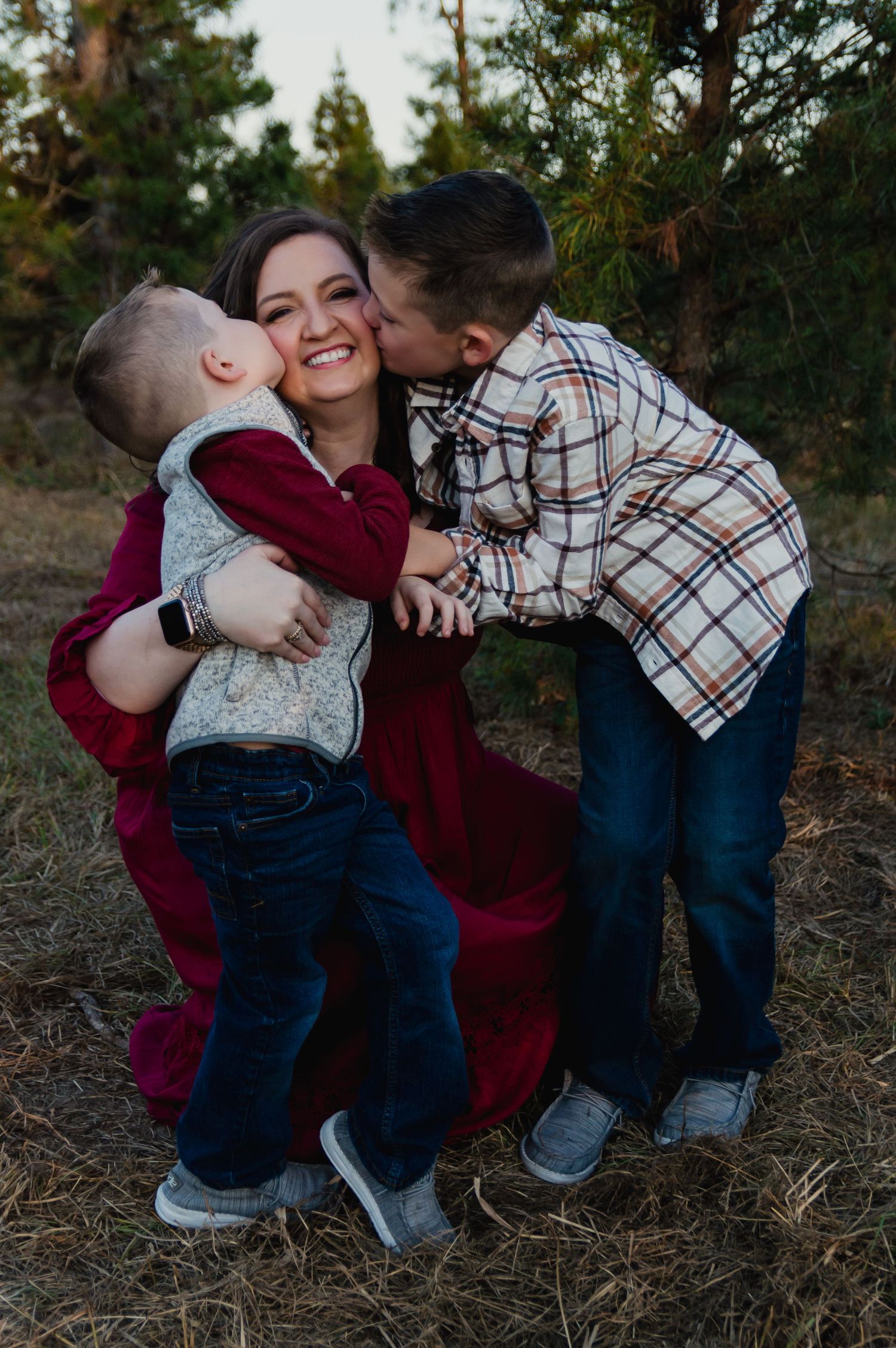 A heartwarming family portrait capturing sweet moments and embraces outdoors against a pine forest backdrop.