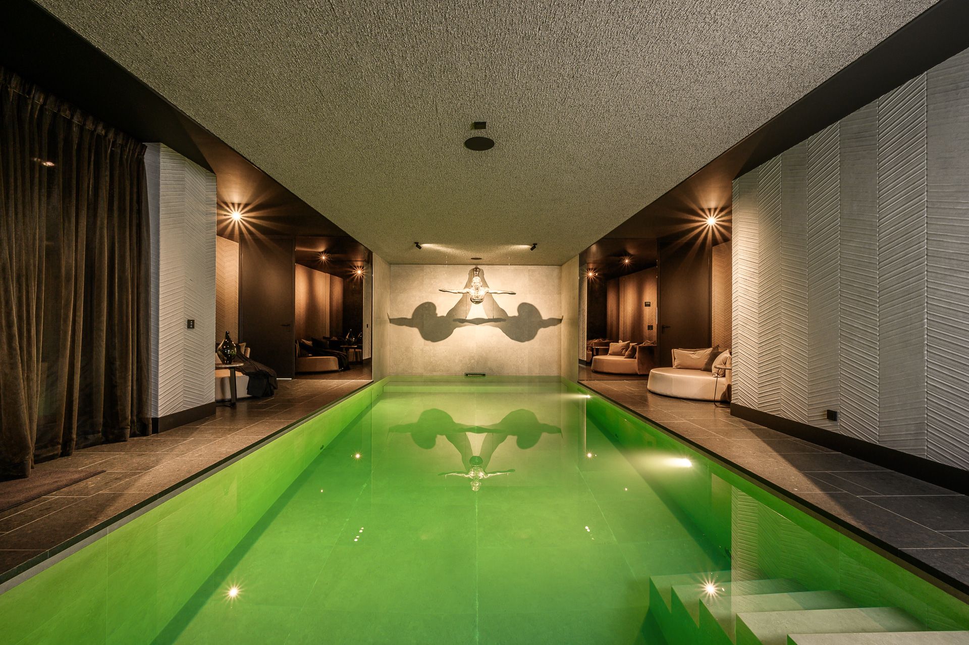 Indoor swimming pool with emerald green water and ambient lighting creating a serene atmosphere.