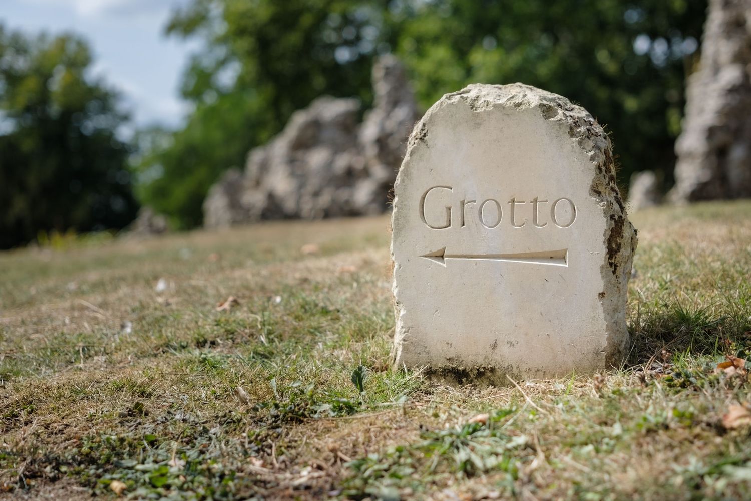 A row of weathered stone gravestones stands in a grassy cemetery under natural lighting, showing age and patina.