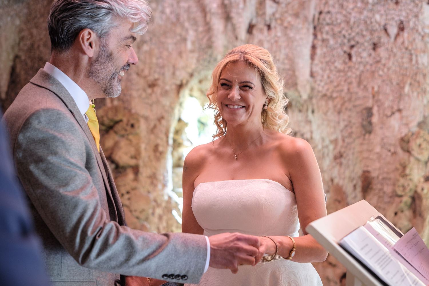 A couple exchanges wedding rings during an intimate outdoor wedding ceremony in a rustic stone setting.