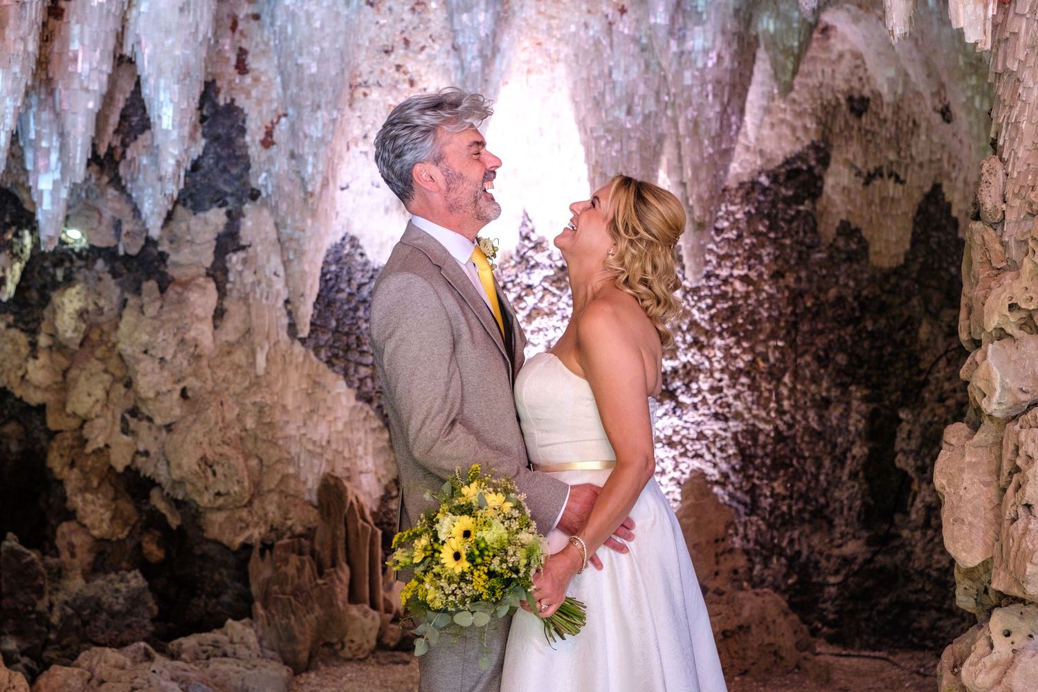 Bride and groom share a romantic moment in front of a rustic stone backdrop at an outdoor wedding ceremony.