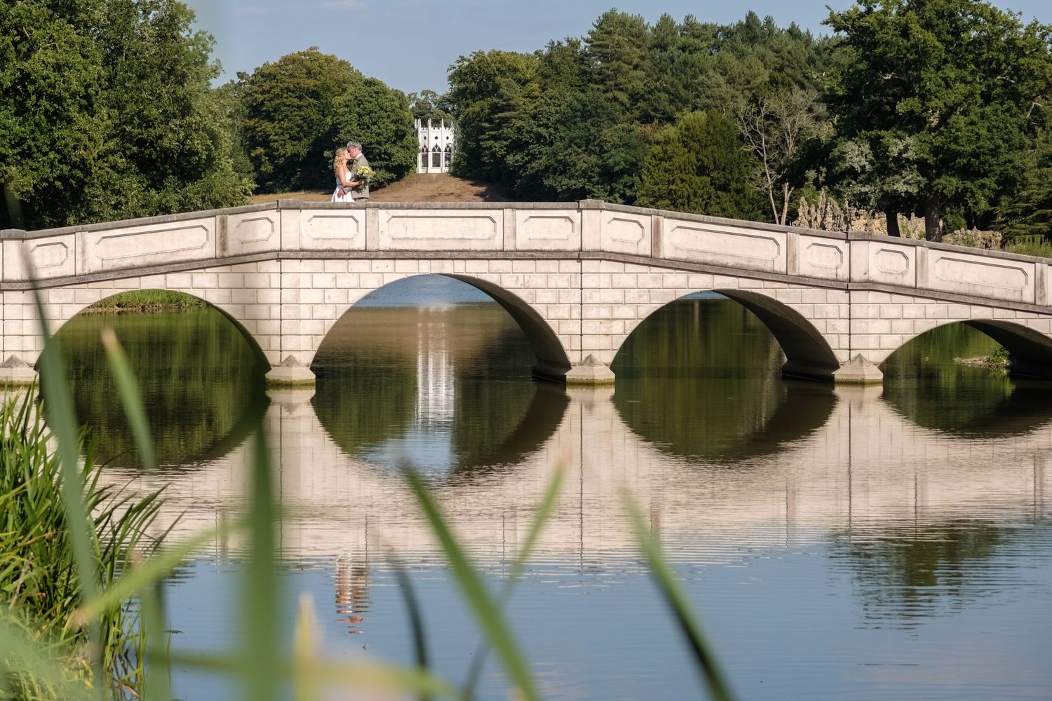 Historic stone bridge with multiple arches reflects beautifully in calm water at Prospect Park, Brooklyn on a sunny day.