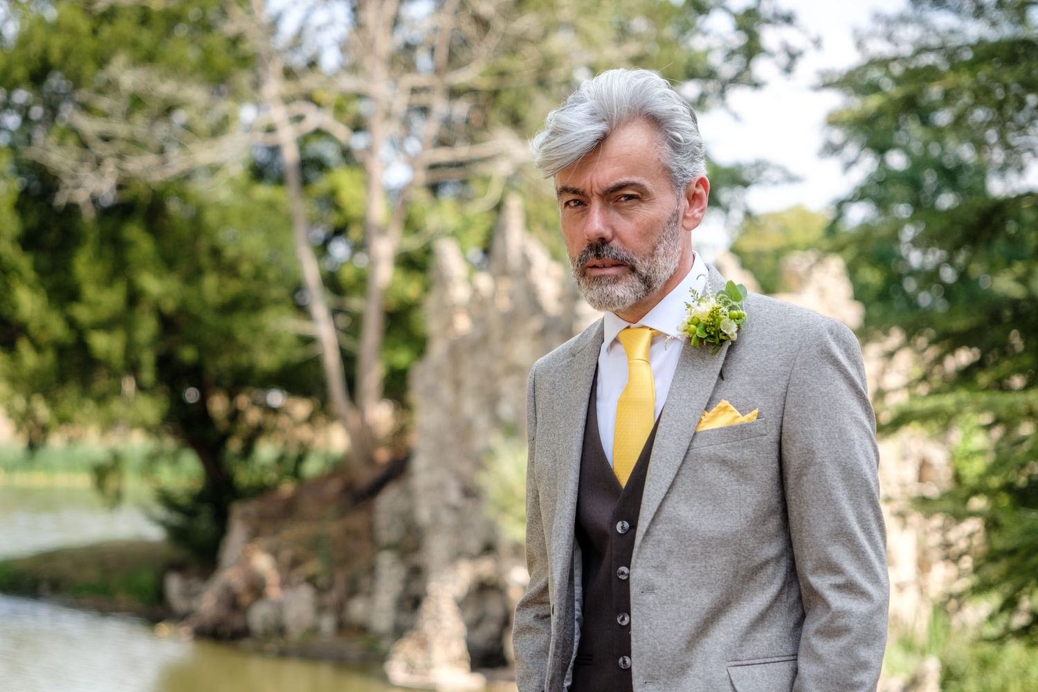 A groom and groomsmen in gray suits pose together outdoors for wedding party photos.