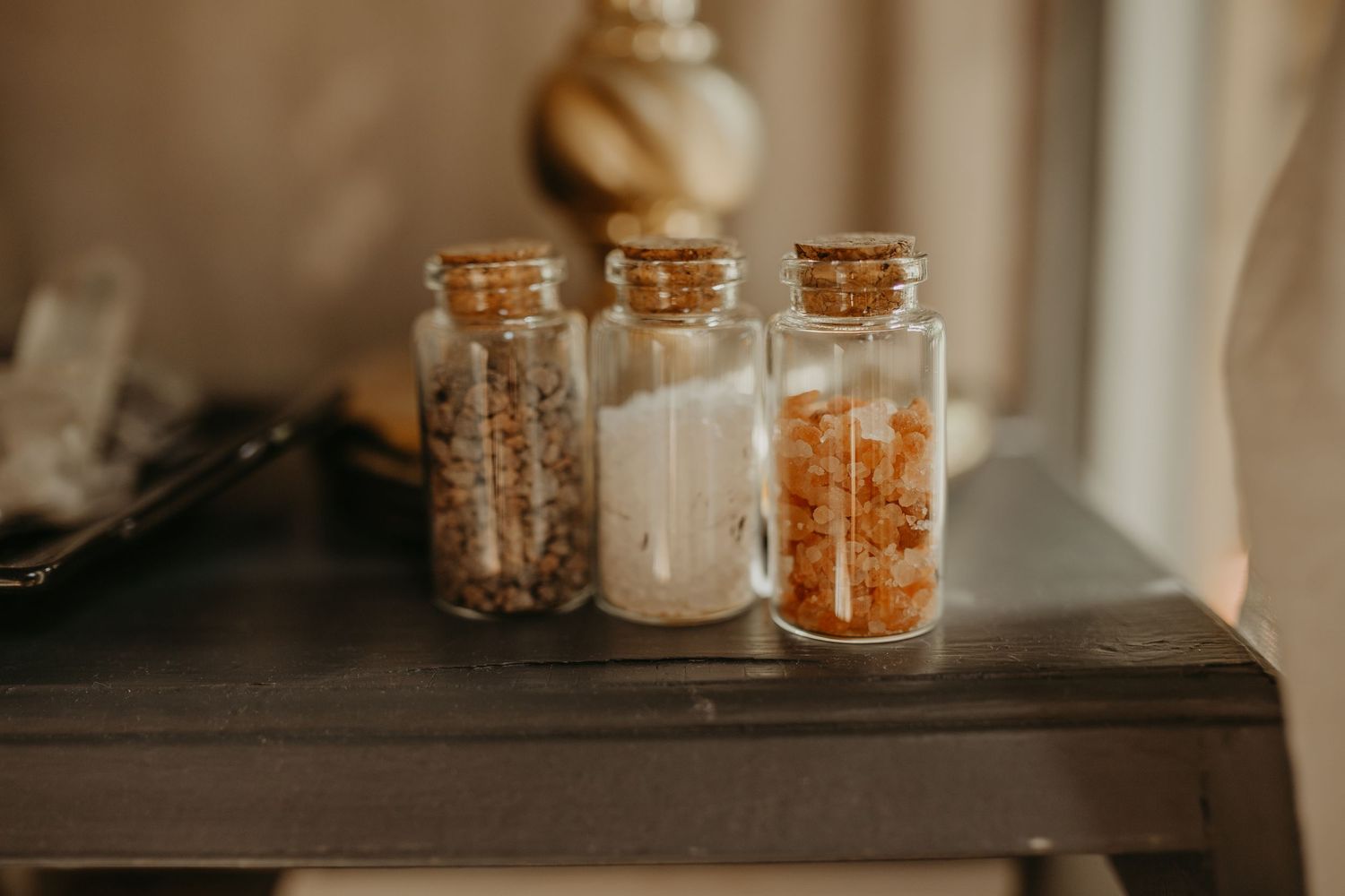 Small glass jars with cork stoppers filled with various dried spices and seasonings arranged on a wooden shelf.