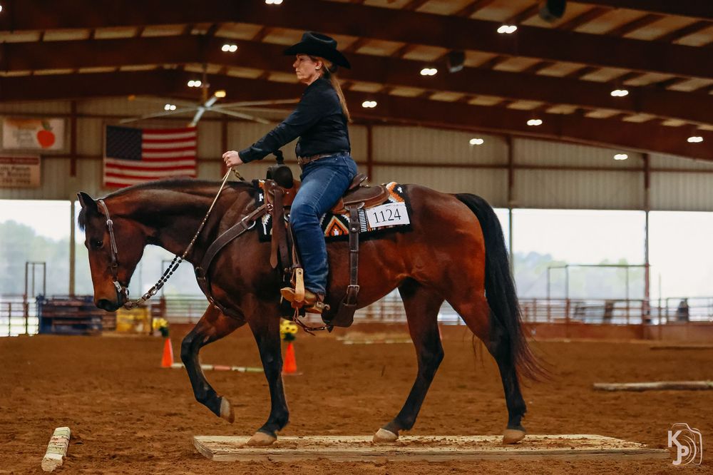 Multiple riders practice horsemanship skills in an indoor equestrian arena with reddish dirt footing.