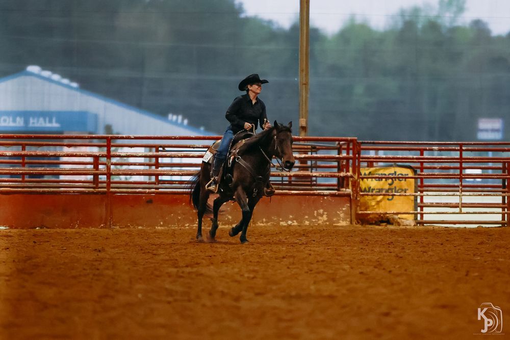 A rider on horseback practices barrel racing in a dirt arena with red metal gates.