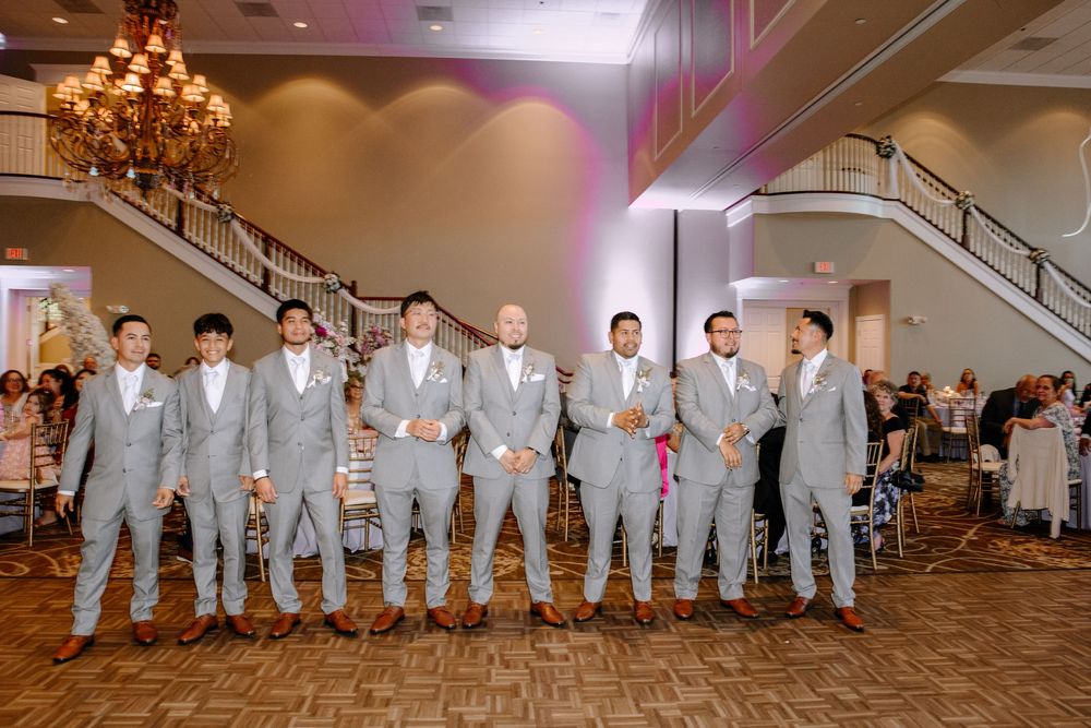 Groomsmen wearing matching light gray suits perform a choreographed dance routine at a wedding reception.