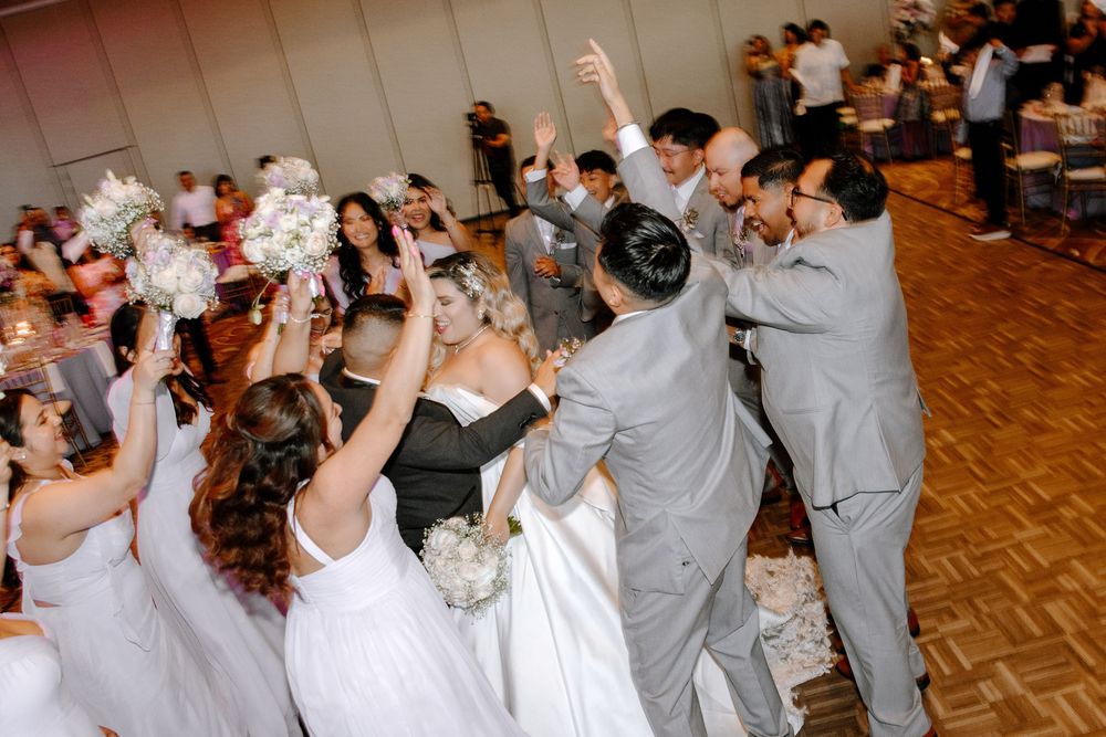 Couples in formal attire dance together at a wedding reception on a parquet dance floor.