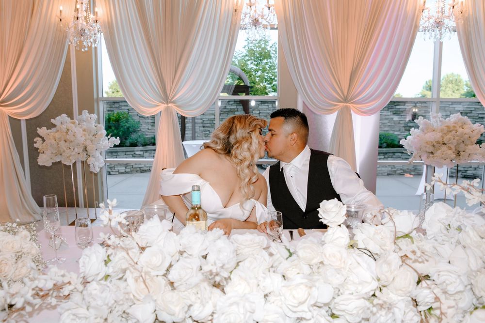 Lavish wedding reception tables with crystal chandeliers, white draping, and elegant floral centerpieces create a romantic setting.