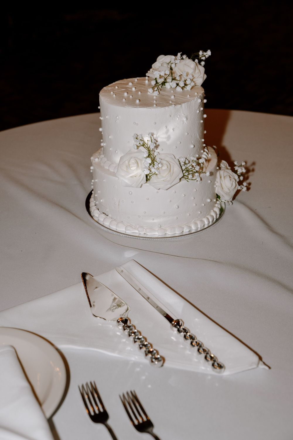 Elegant two-tiered white wedding cake with delicate floral decorations and serving utensils on a crisp white tablecloth.