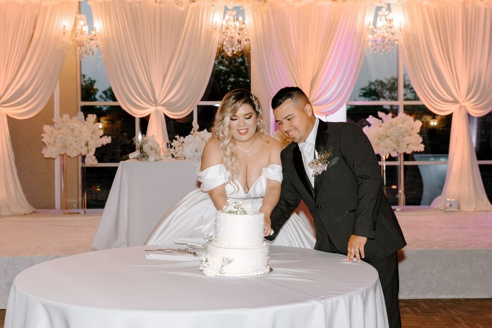 A wedding reception venue with white drapes, illuminated chandeliers, and pink uplighting creates an elegant atmosphere.
