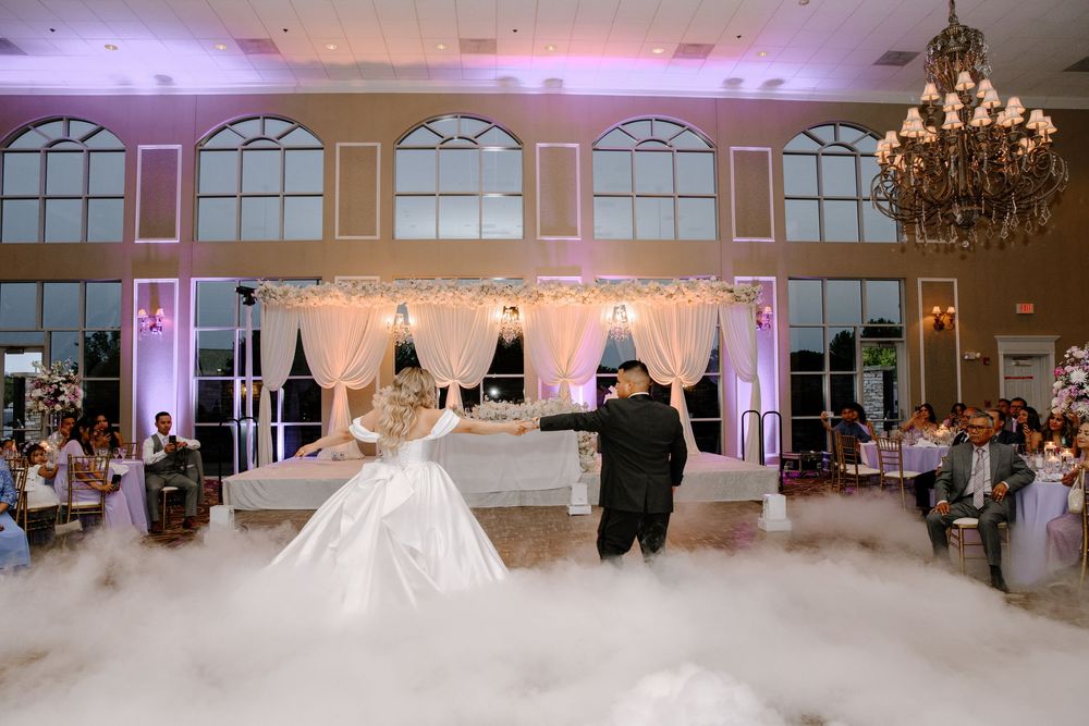 Wedding guests dance on a foggy dance floor with elegant uplighting at an indoor ballroom reception venue.