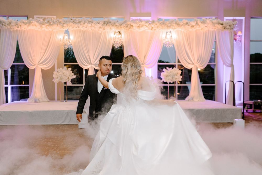 Ballroom dance floor illuminated with soft pink lighting and surrounded by white fabric draping and elegant decor.