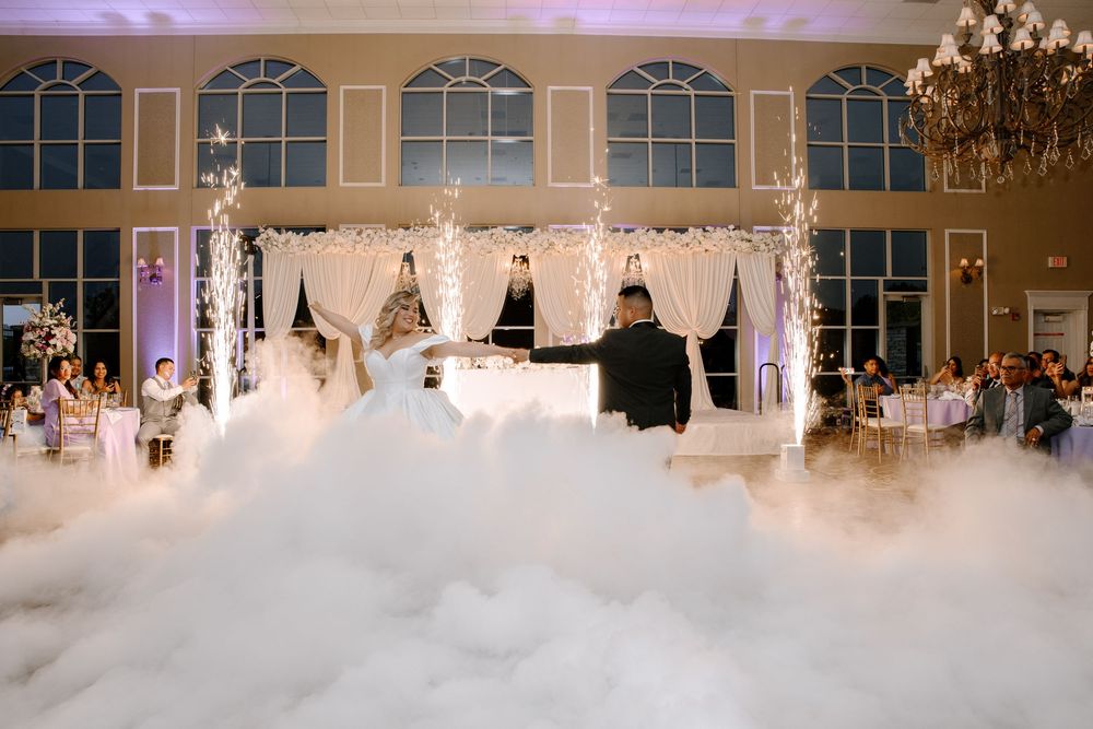 During a wedding reception at an elegant venue, fog machines create a dreamy dance floor atmosphere under chandeliers.