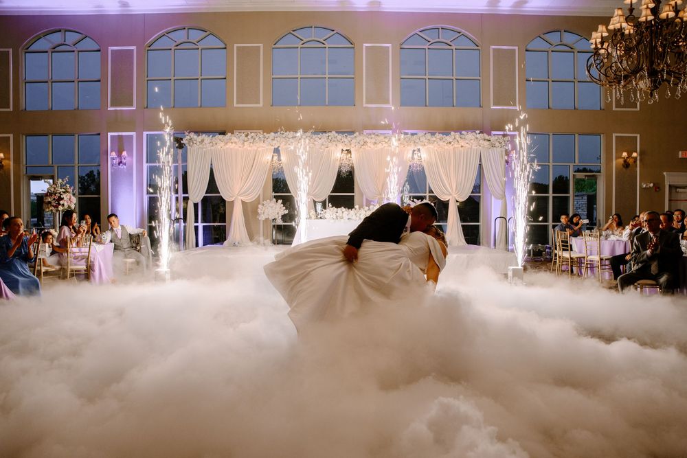 A dramatic fog effect billows across a wedding venue floor while guests gather around elegant displays.