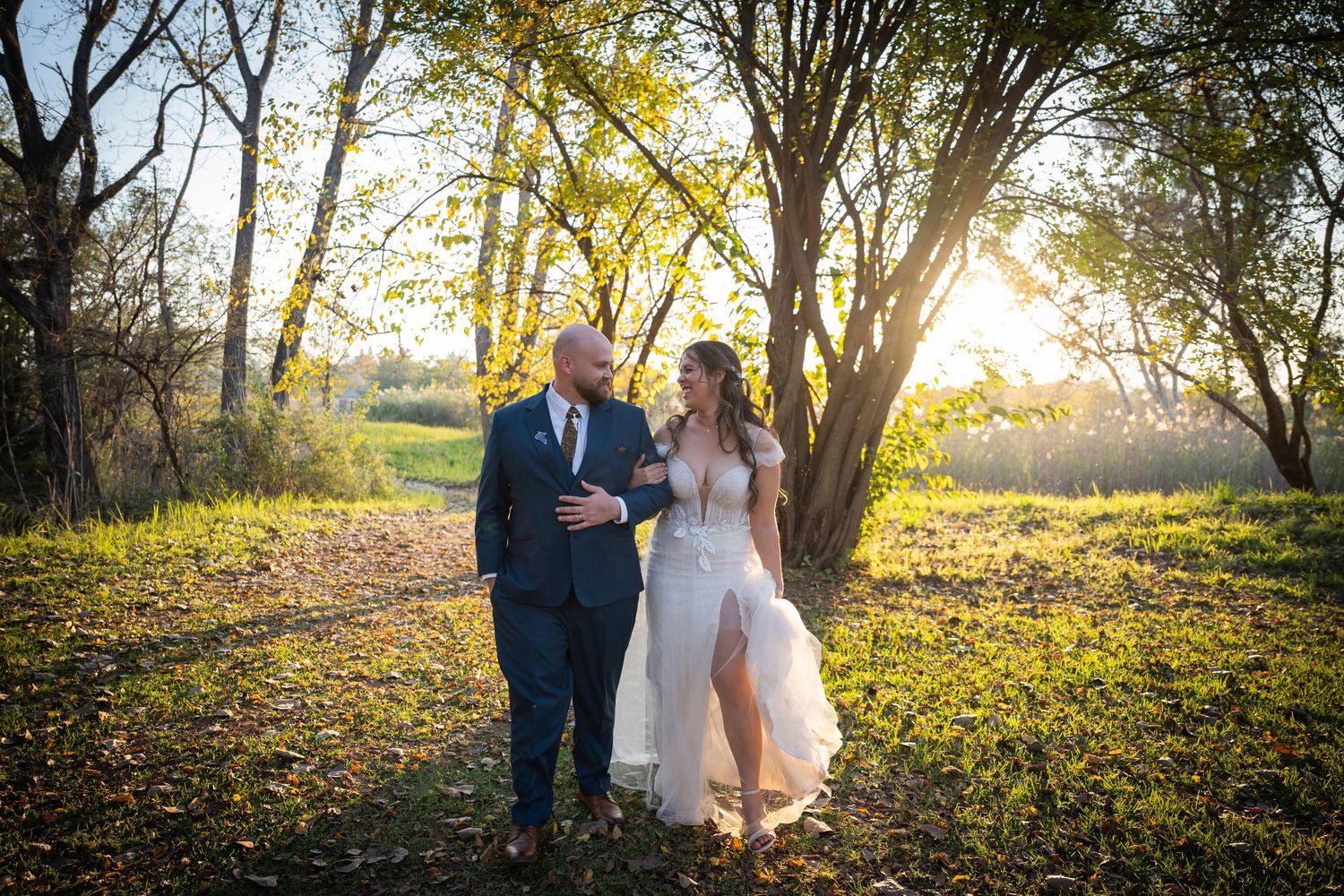 Romantic autumn wedding photos taken outdoors with golden sunlight filtering through trees and fallen leaves.