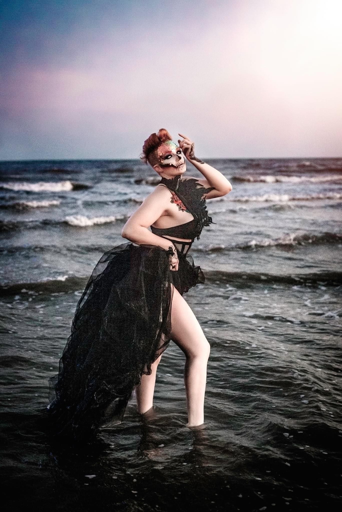 Moody seaside photoshoot with waves crashing against dark rocks at sunset.
