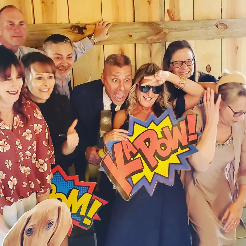A group of people posing together with comic book style POW graphics overlaid on a fun photo in a wooden interior.