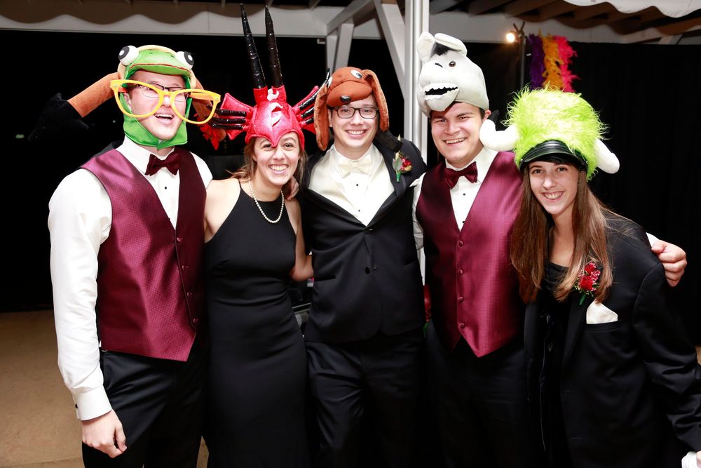 Group wearing maroon and black formal attire poses with festive party props at a photo booth event.