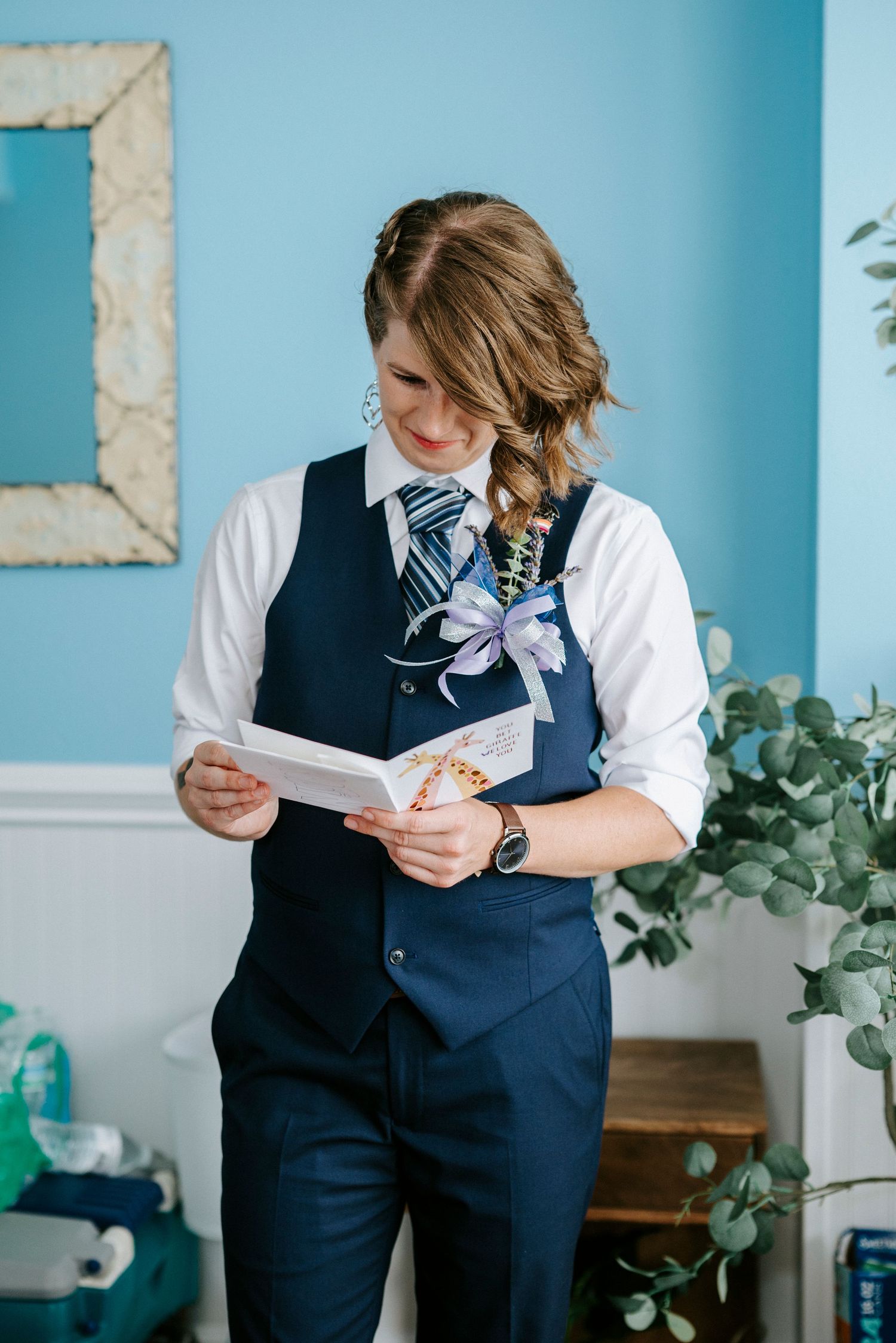 A person in a navy vest and white shirt reads a letter in a room with blue walls.