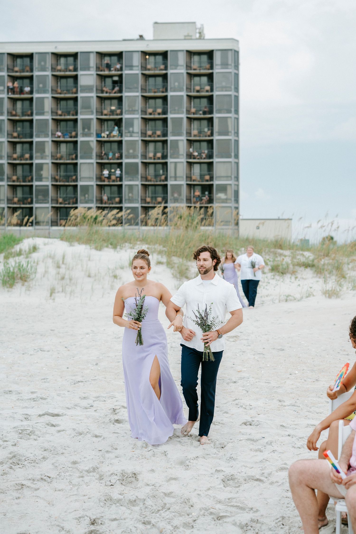Fun candid moments of guests playing in the sand at a beachfront wedding with condos in the background.