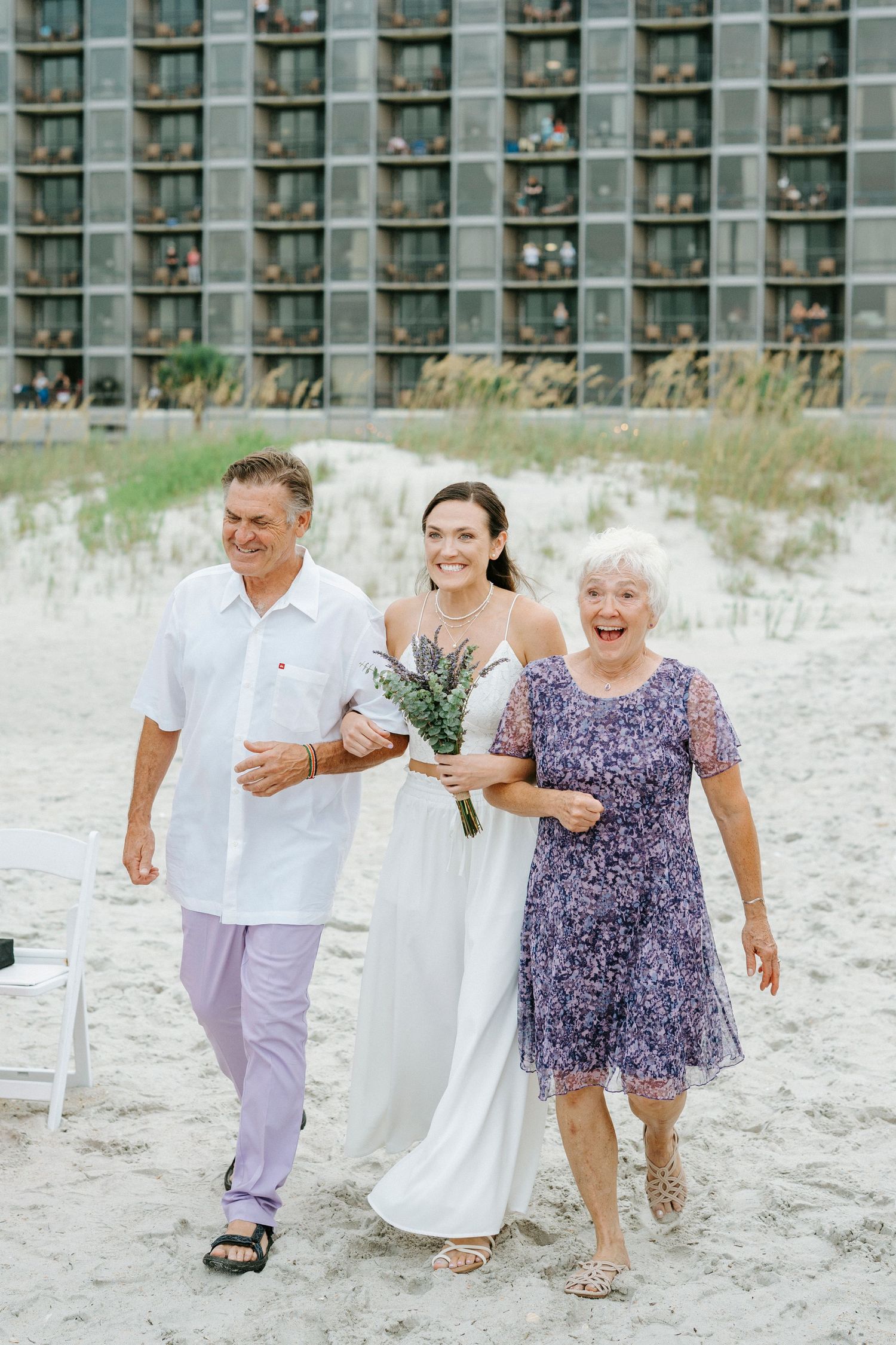 Wedding party joyfully runs and plays together on a sandy beach.