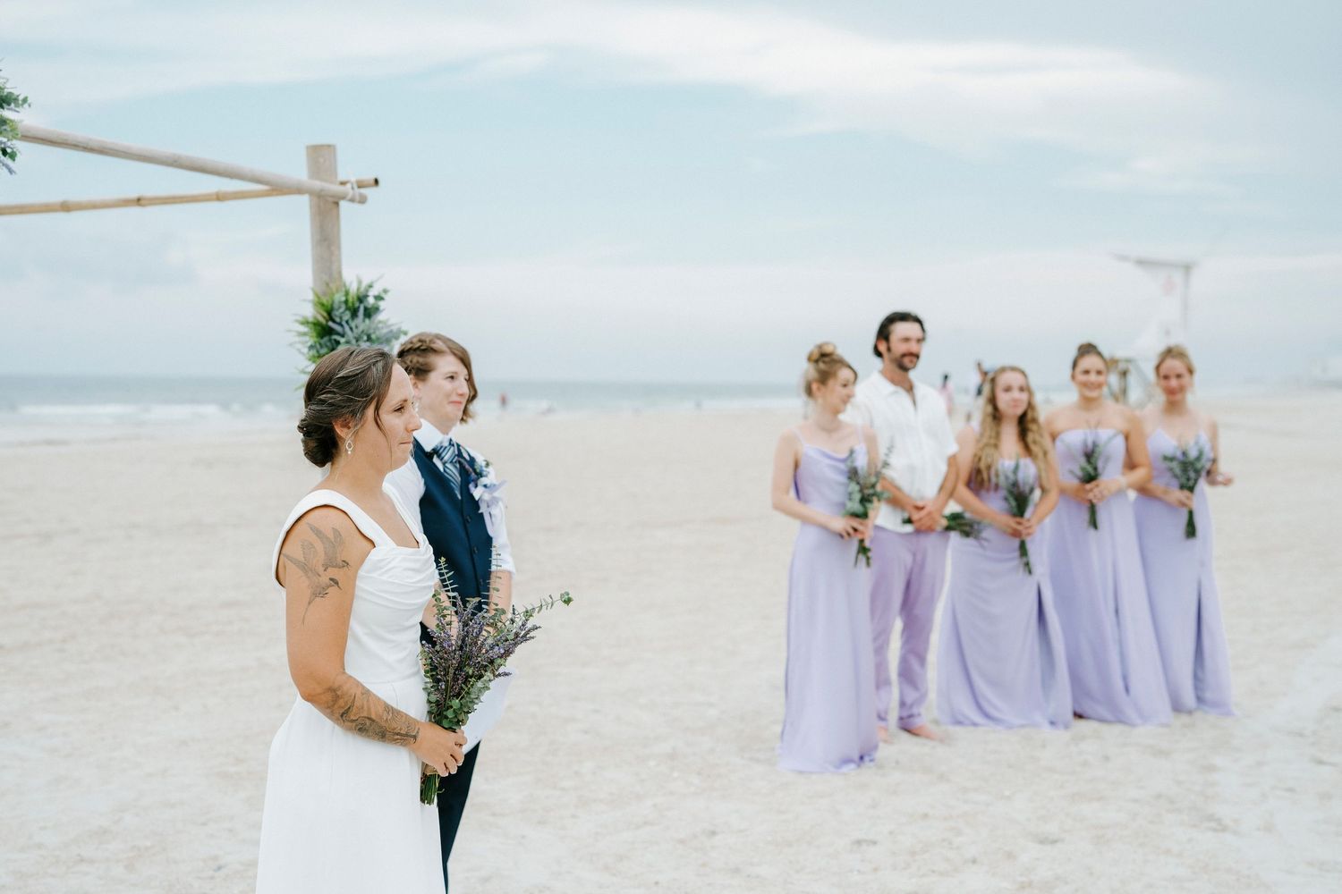 A beachside wedding ceremony setup with bridesmaids in lavender dresses.