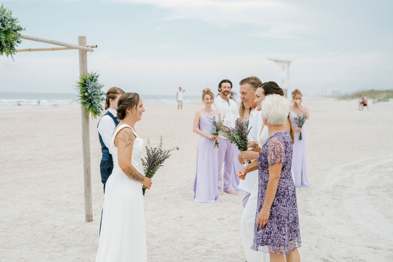 Simple beach wedding setup with white and purple decor on a sunny day.