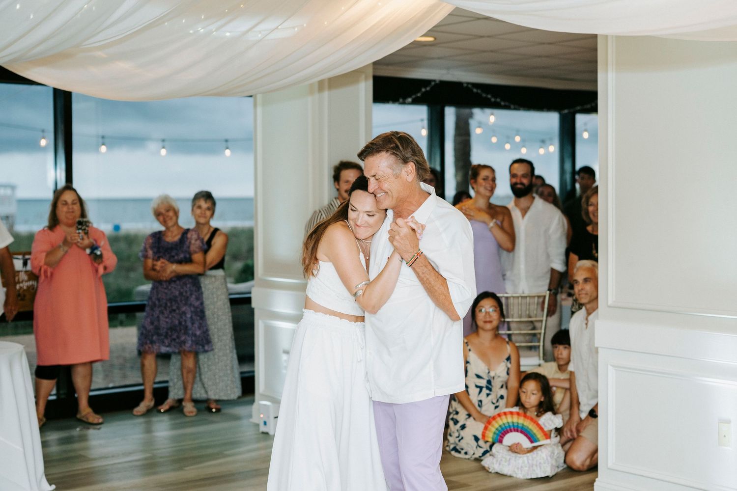 Couple shares their first dance at a beachside wedding reception while guests watch and smile.
