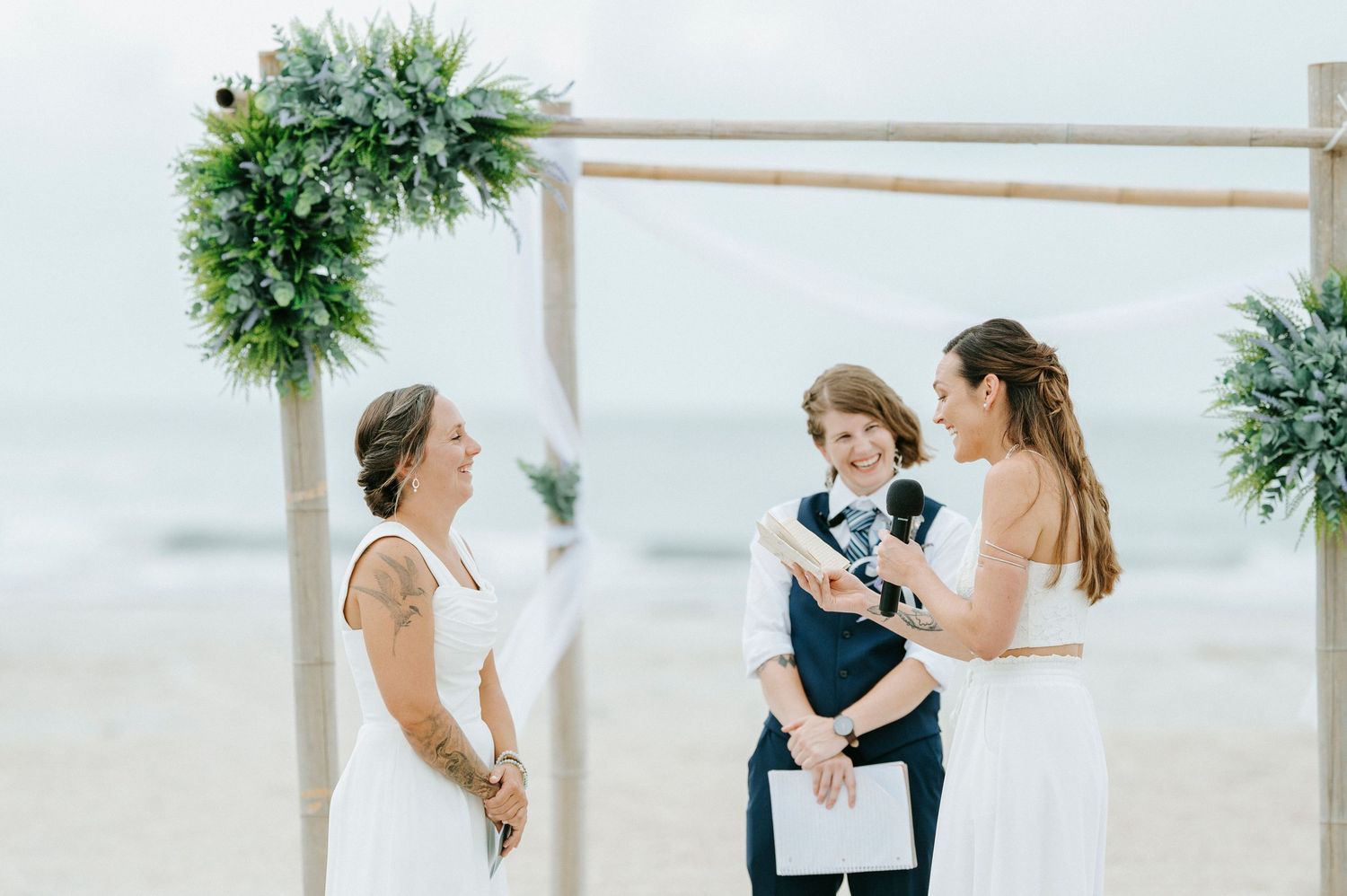 A couple shares a romantic moment during their beach wedding ceremony while surrounded by greenery.