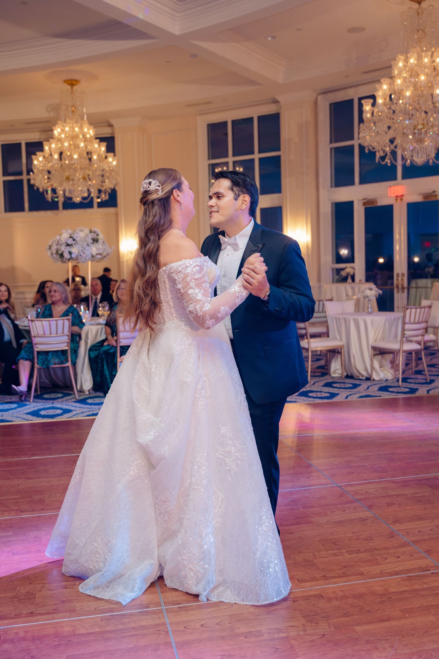 A couple shares their first dance as newlyweds in an elegant ballroom with crystal chandeliers and hardwood floors.