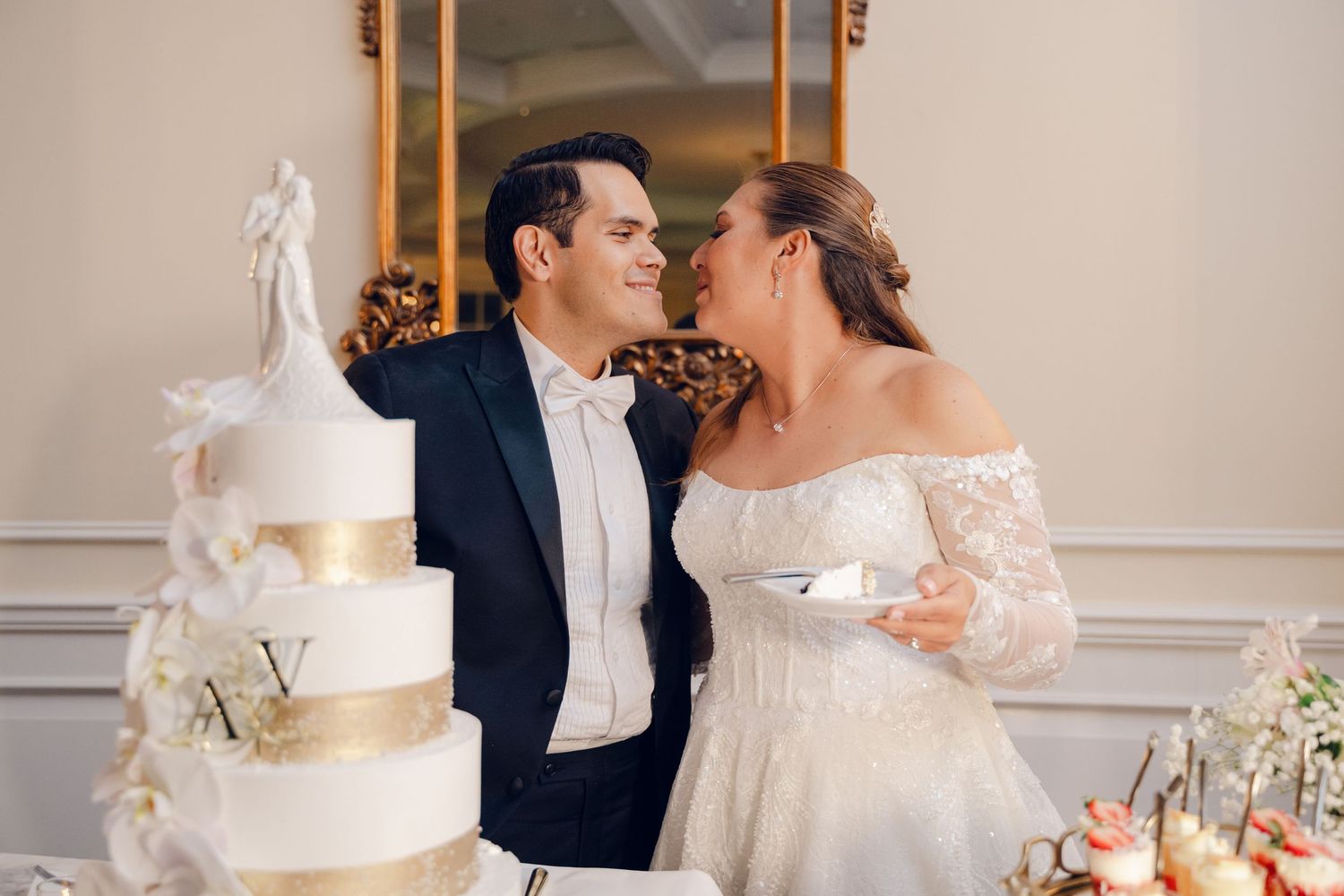 Elegant wedding reception features white tiered cake adorned with delicate floral decorations and romantic couple moment.