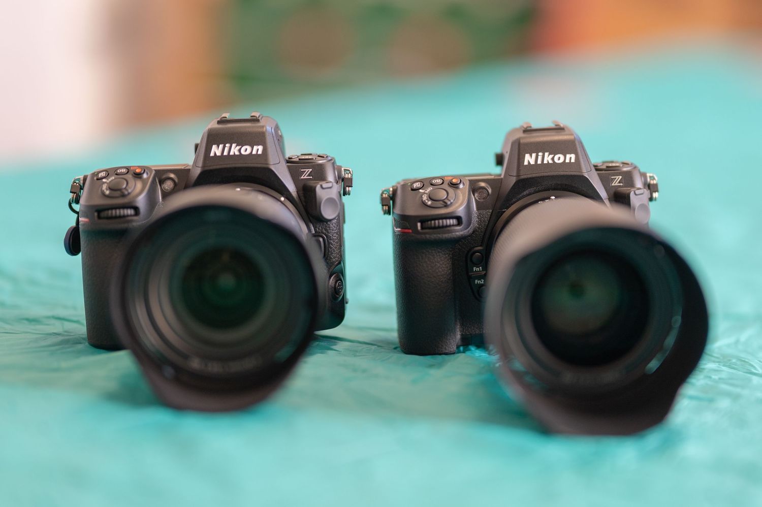 Two Nikon cameras with large lenses positioned side by side on a turquoise surface with shallow depth of field.