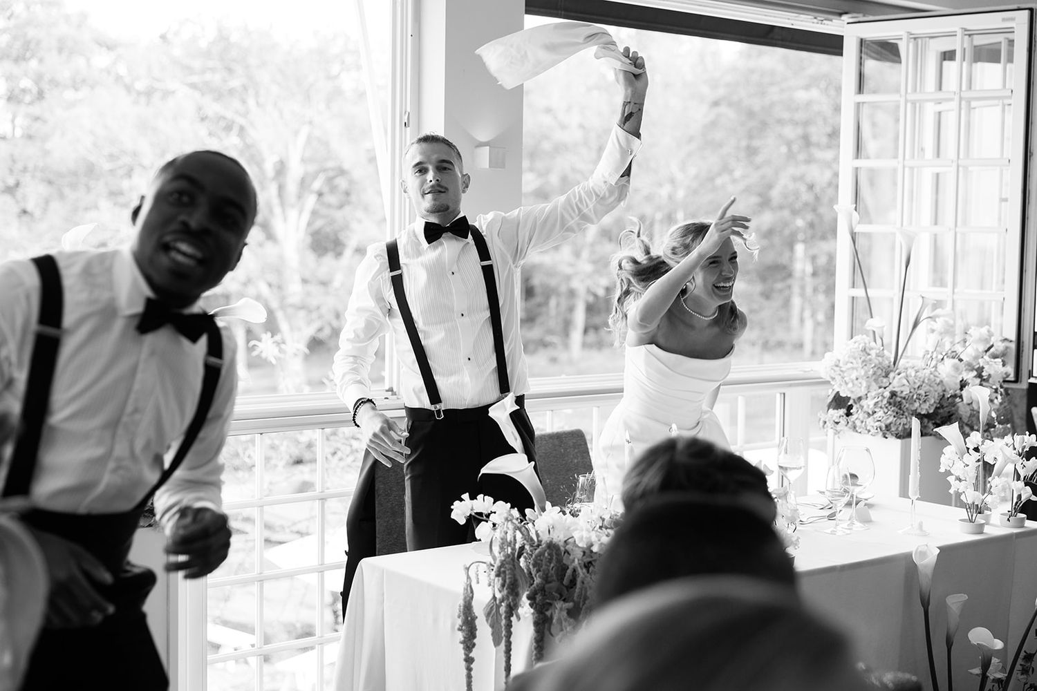 Black and white photo of a wedding celebration with people dancing and socializing in an indoor venue.