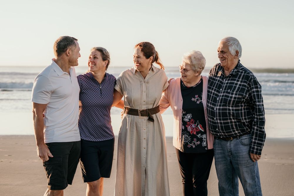 Group of five family members smiling together on sunny beach with ocean waves in the background.