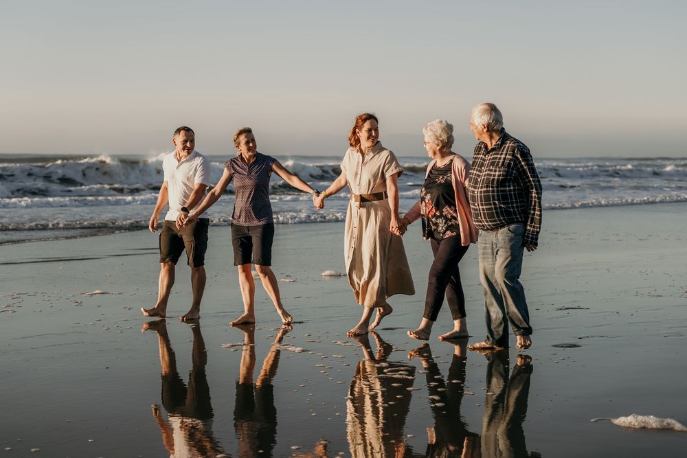 Happy family of five walking hand-in-hand along reflective wet beach shoreline at golden sunset.