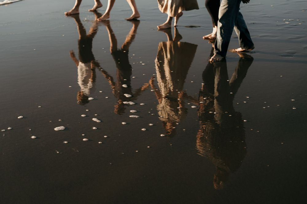Reflections of five people walking barefoot on wet beach sand captured in artistic low-angle shot.