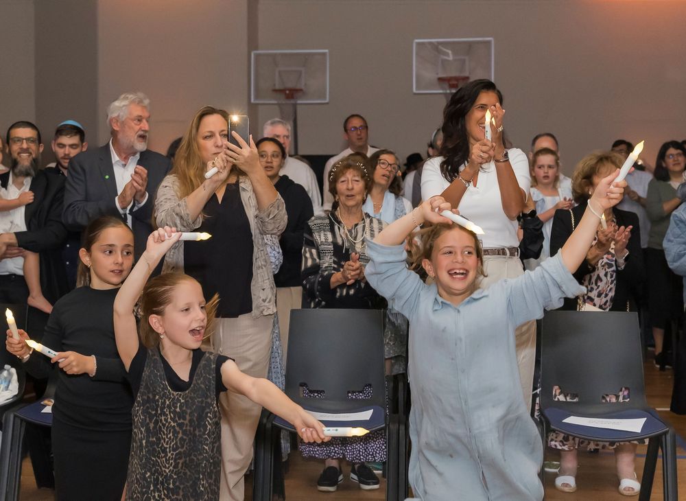 Crowd of people celebrating and cheering enthusiastically in an indoor venue with basketball hoop visible in background.