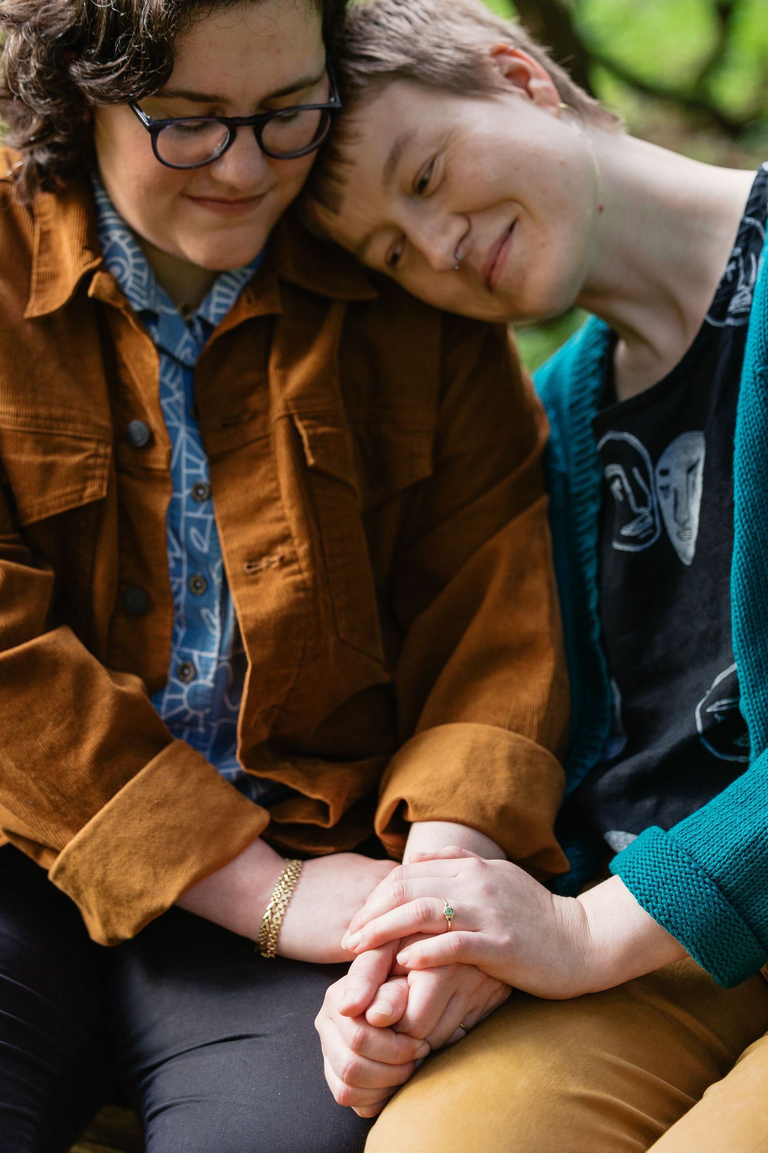 Two women sitting closely together holding hands tenderly beneath a tree in soft natural light.