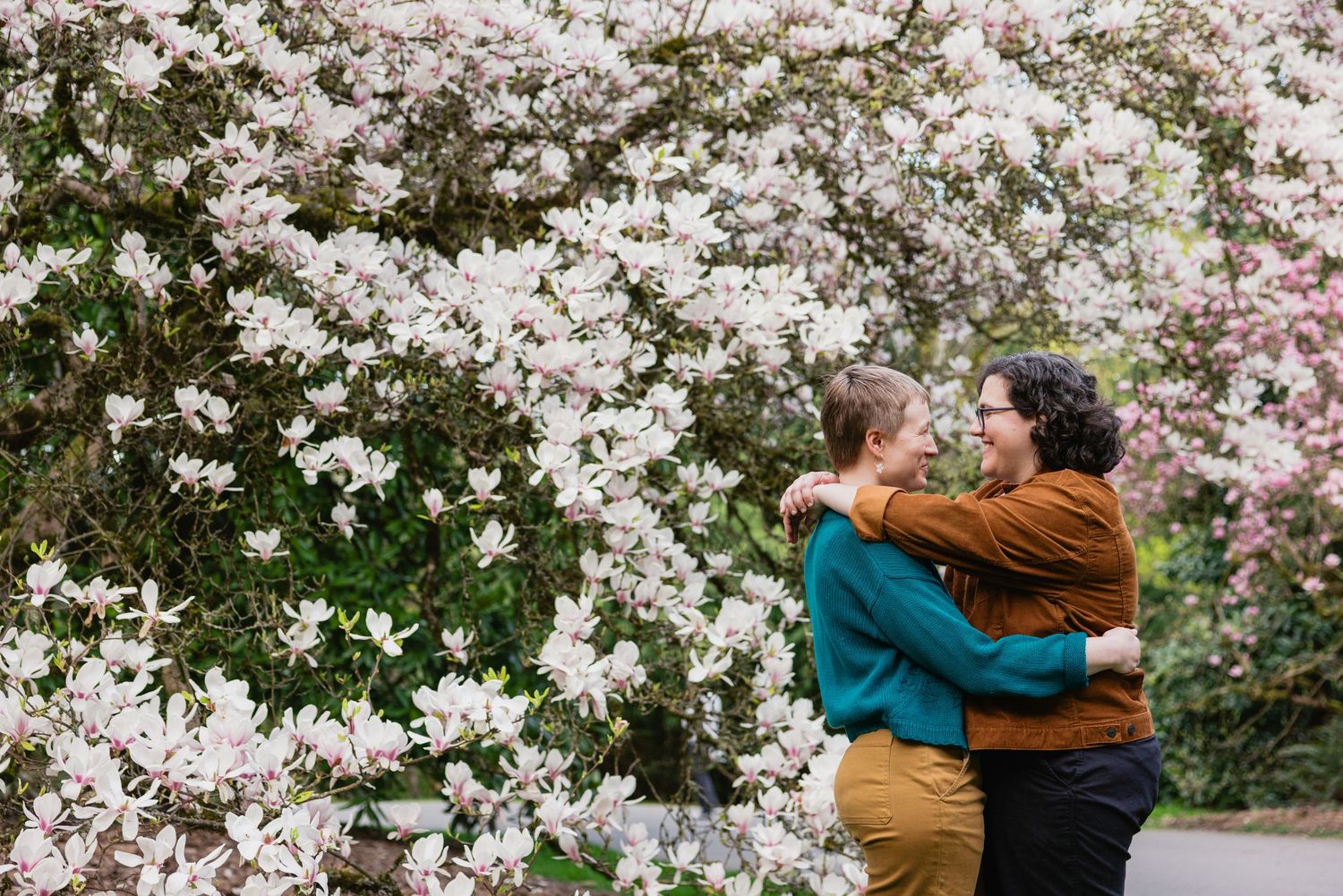 Couple embracing in front of blooming white magnolia flowers in a garden during spring.