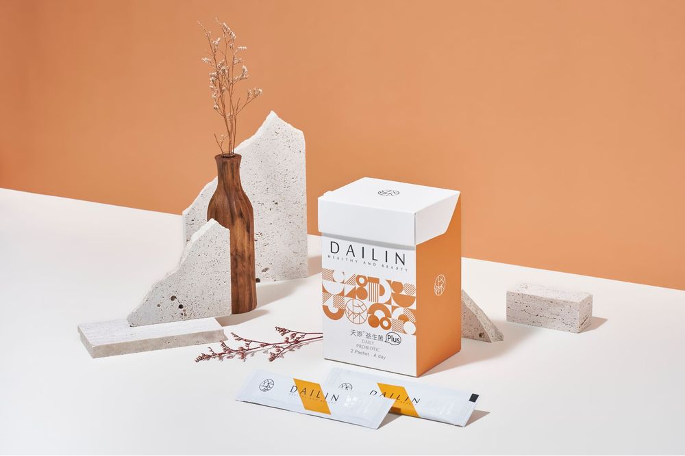 Minimalist product packaging display with dried branches and white boxes against a warm orange background.
