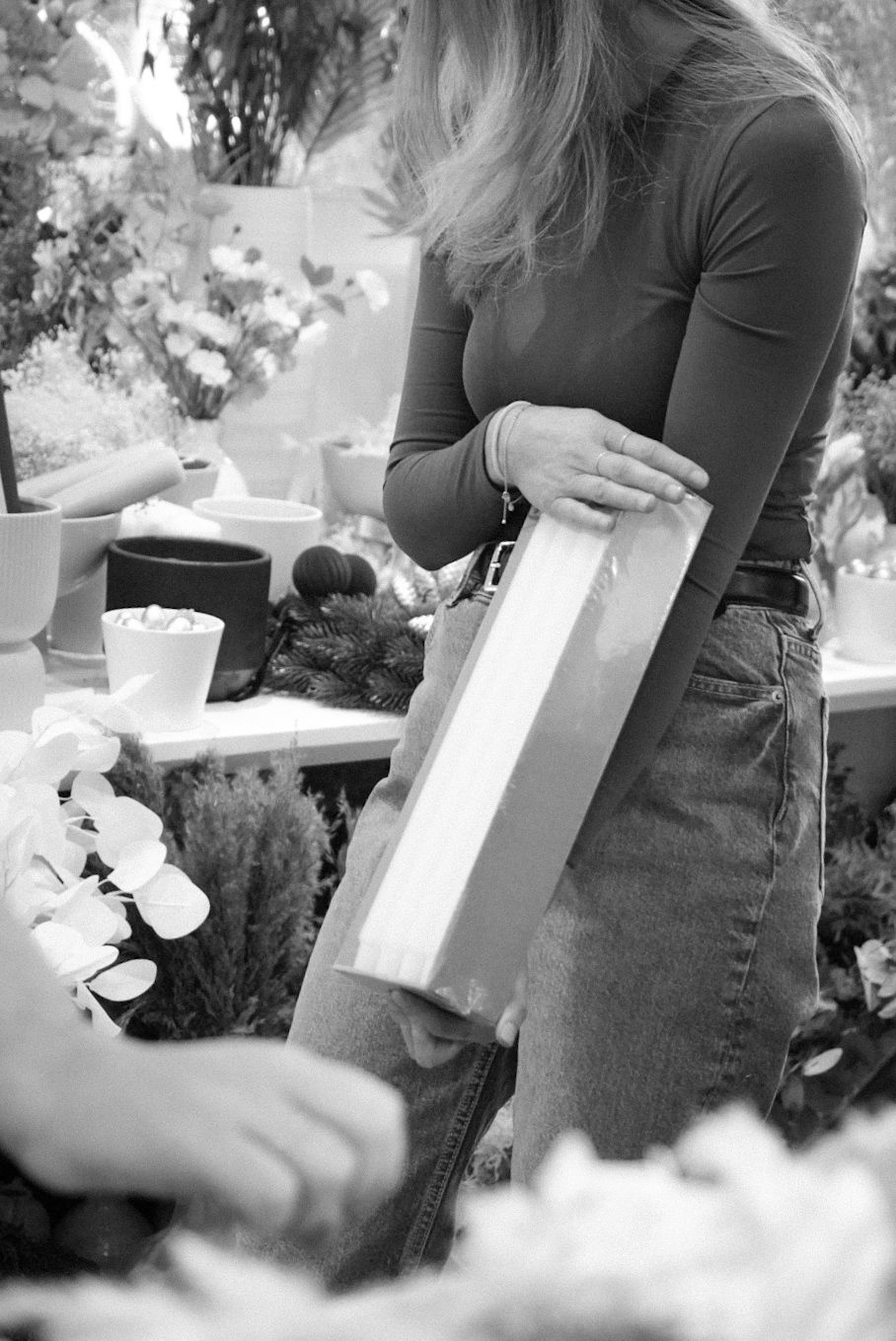 Black and white image of someone holding a tall container among flowers and tea settings.