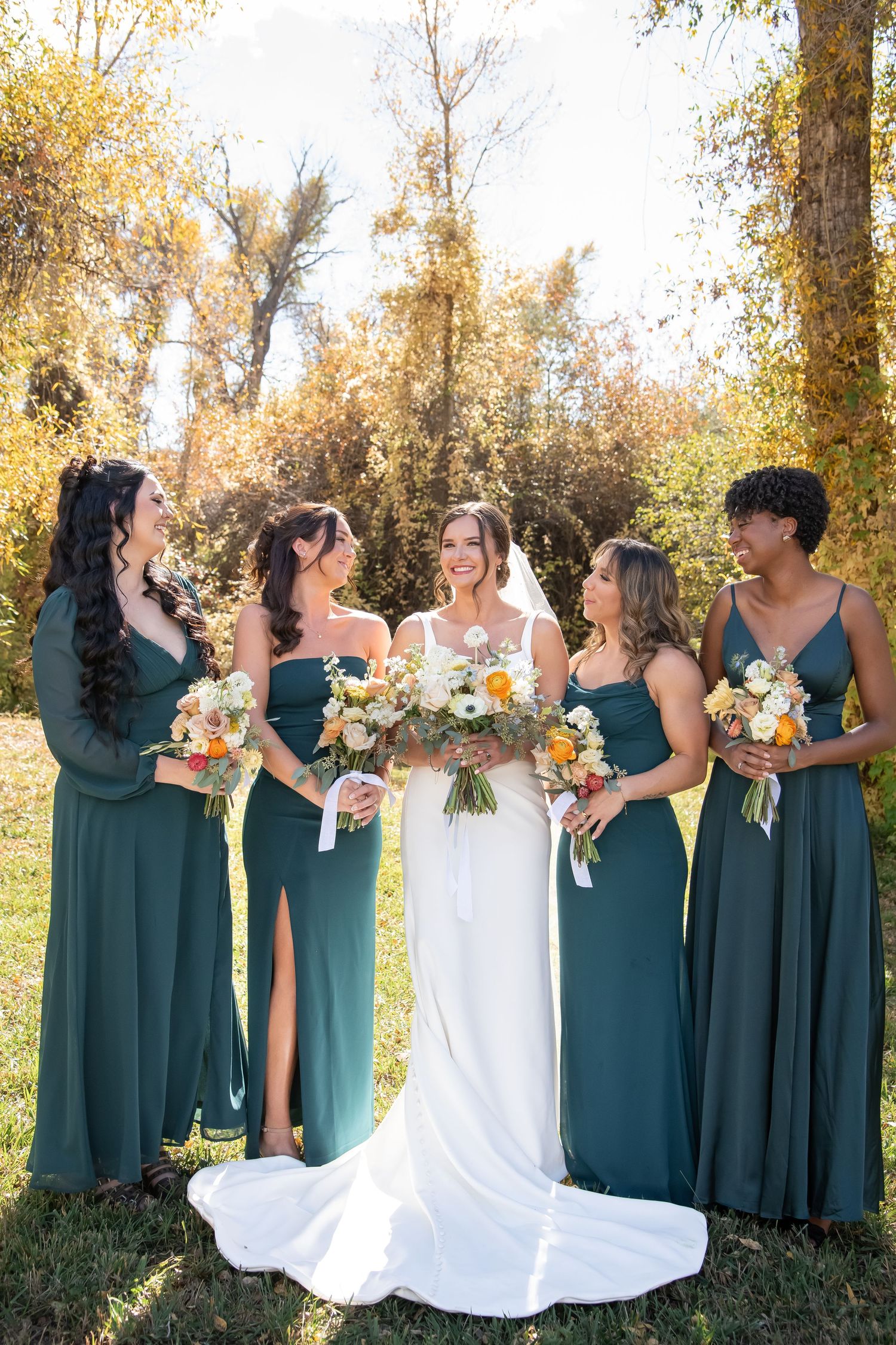A bride in a flowing white gown poses gracefully on a green lawn with elegant blue and white floral arrangements at fall wedding Vail
