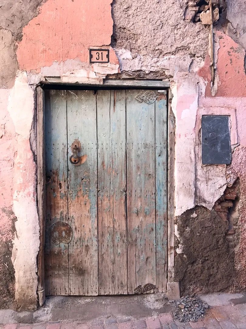 A worn turquoise wooden door set in an aged pink plaster wall with cracked textures.