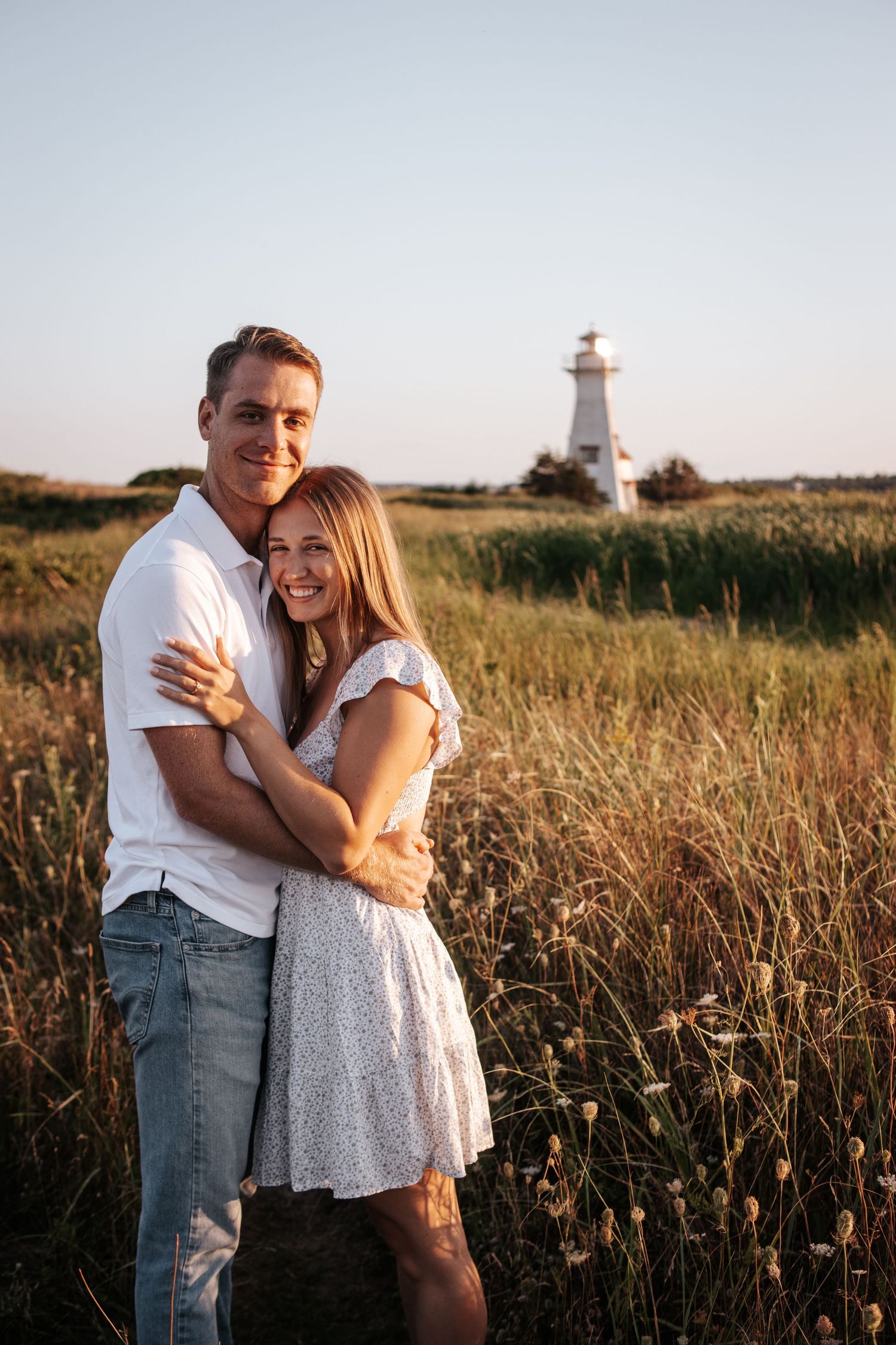 A couple in white outfits shares a romantic moment together during a sunset photoshoot in a natural outdoor setting.