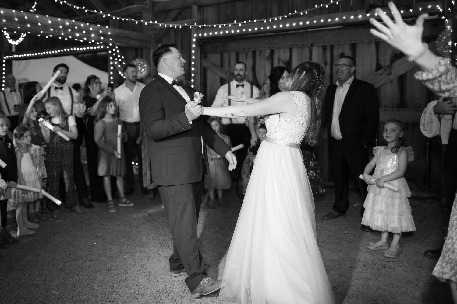 Wedding couple shares their first dance on a reception floor illuminated by twinkling string lights above. Wedding photographer WI MN