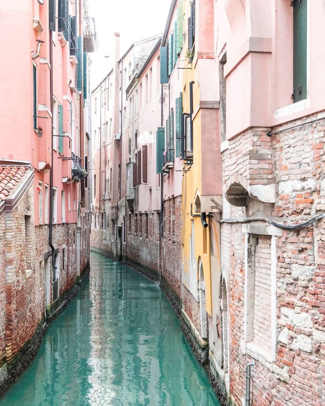 Venetian canal lined with colourful weathered buildings reflected in turquoise water.